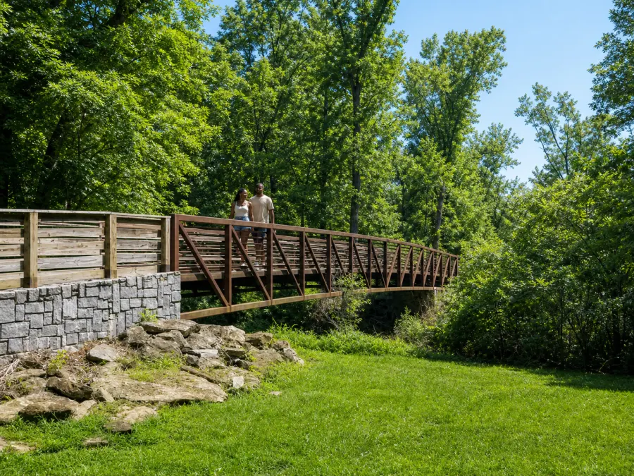 A couple walking across the steel trail footbridge in the Lionel Hampton-Beecher Hills Nature Preserve.