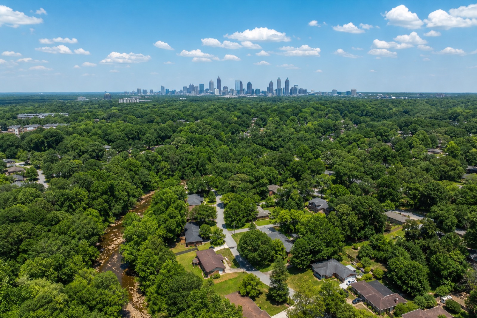 Aerial view at golden hour over southwest Atlanta's rolling tree canopy, rooftops showing through the green, with the downtown skyline on the horizon.